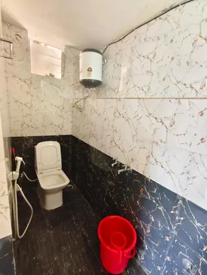 a bathroom with a toilet and a red bucket at MISTY cottage in Ooty