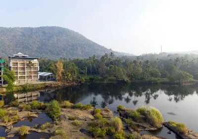 a river with a building next to a mountain at River Bay Athirappilly in Athirappilly
