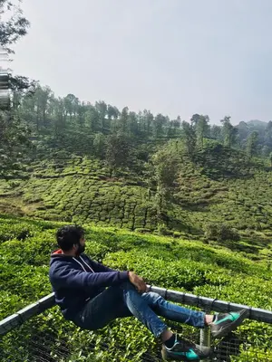 a man sitting on a rail in front of a tea plantation at Boche LuxCamp 1000 Acre in Wayanad