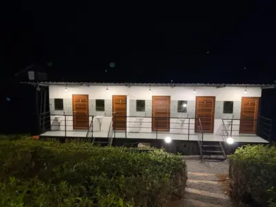 a white building with wooden doors at night at Boche LuxCamp 1000 Acre in Wayanad