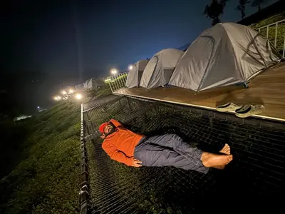 a man laying on top of a fence at night at Boche LuxCamp 1000 Acre in Wayanad