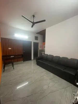 a living room with a black couch and a ceiling fan at Mountholidays in Meppādi