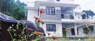 a white house with red flowers in front of it at Surya Homestay in Marayoor