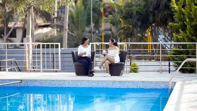 two women sitting in chairs next to a swimming pool at Bombe Resort Channapatna in Channapatna