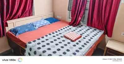 a small bedroom with a bed with red curtains at Hazel's ELiTE Homestay 3BHK in Mysore