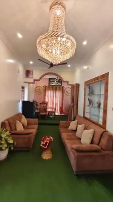 a living room with brown leather couches and a chandelier at Steeva Guest house in Mysore