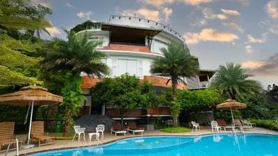 a building with a swimming pool and chairs and umbrellas at Mount Xanadu Resorts in Ambalavayal