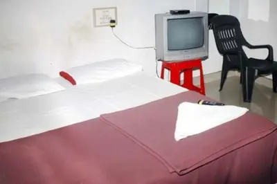 a room with a bed and a tv and a chair at Hotel Ashwini Lodge in Mysore