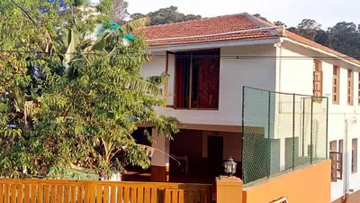 a white house with a fence and a tree at Satya Anand Cottage Pure Veg and Non Alcoholic Hotel in Coonoor