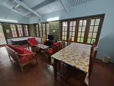 a dining room with a table and chairs and windows at Green Acres Farm Guest House in Masinagudi