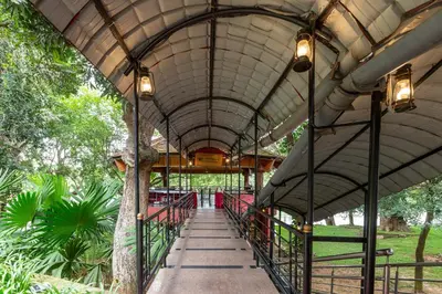 a covered walkway in a park with a building at KSTDC Hotel Mayura Riverview Srirangapatna in Seringapatam