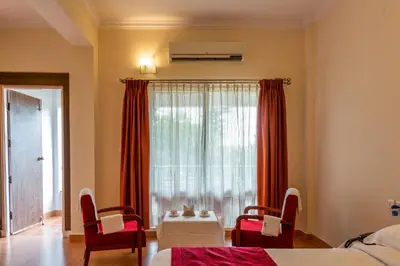 a bedroom with a bed and chairs and a window at KSTDC Hotel Mayura Kauvery KRS in Hosa Kannambādi