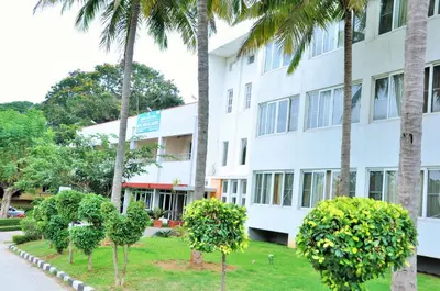 a white building with palm trees in front of it at KSTDC Hotel Mayura Kauvery KRS in Hosa Kannambādi