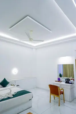 a white bedroom with a bed and a chair at Casino Hotels Ltd in Trichūr