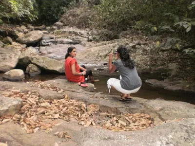 two women sitting on rocks near a stream at Vacanza Estate House in Kakkabe