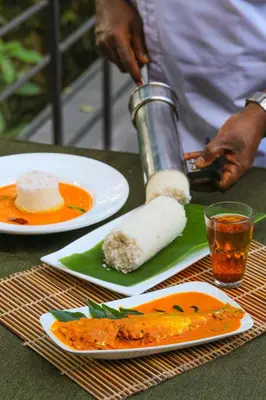 a person preparing food on a table with plates of food at Wayanad Wild - A CGH Earth Experience in Vythiri