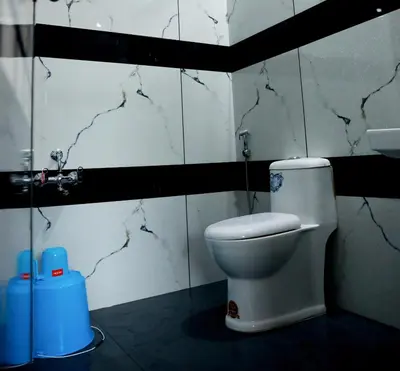 a bathroom with a white toilet and marble walls at Green Garden Jasmin Cottage in Vayittiri