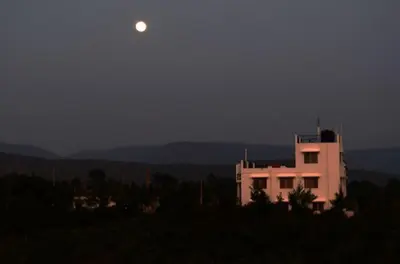 a moon rising over a white building at night at Green Peace Bheemeshwari in Halgūr
