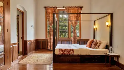 a bedroom with a canopy bed and a window at SaffronStays Milton Abbott Estate - 2BR colonial-era bungalow with garden, golf course views & bonfire nights near Ooty Golf Club in Ooty