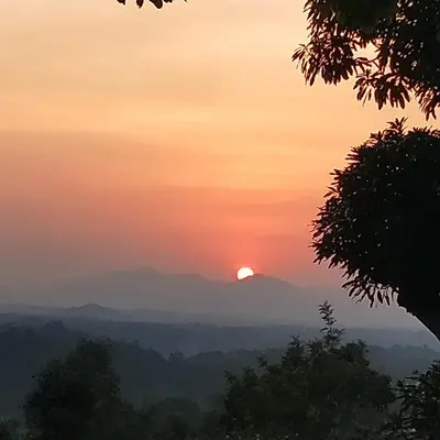 a sunset in the mountains with the sun in the sky at Forestdale Coorg in Virajpet