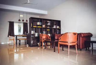 a living room with chairs and a table and a book shelf at Forestdale Coorg in Virajpet