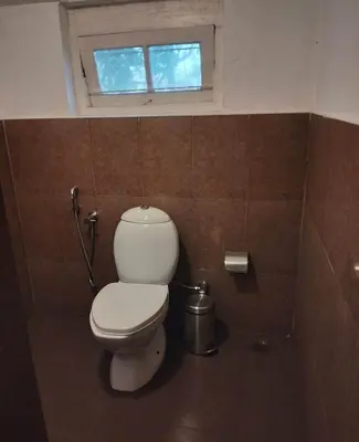 a bathroom with a toilet and a window at Puthuthottam Annexe in Vālpārai