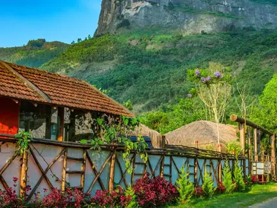 a house with flowers in front of a mountain at Deshadan Eco Valley Resort - An Eco friendly Mud House in Kanthalloor