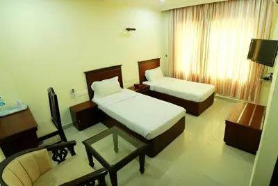 a hotel room with two beds and a chair and a table at Hotel Horizon International in Guruvāyūr