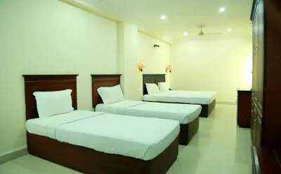 two beds in a hotel room with white walls at Hotel Horizon International in Guruvāyūr