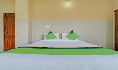 a bedroom with a white bed with green pillows at Treebo Green Land Coorg in Kushālnagar