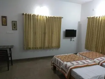 a room with two beds and a desk and a television at Aashraya Homestay in Mysore