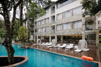 a hotel swimming pool with white chairs and a building at Elixir Hills Suites Resort and Spa in Munnar