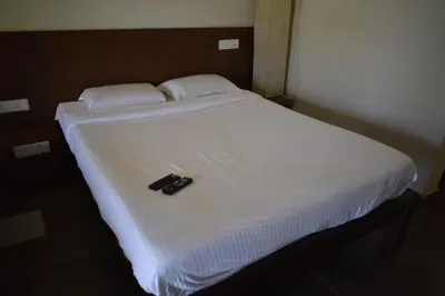 a white bed with a black remote control on it at River Valley Resort in Masinagudi