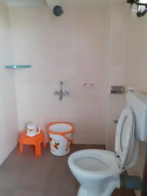 a bathroom with a white toilet and a orange stool at Hotel Paradise Inn in Tiruppūr