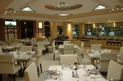 a restaurant with white tables and chairs and people in the kitchen at Sandesh Pride in Mysore