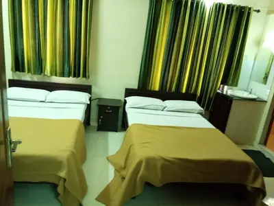 two beds in a hotel room with yellow curtains at Anandkrishna Residency in Guruvāyūr