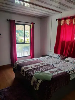 a bedroom with a bed with red curtains and a window at ExoticaHolidays in Sultan Bathery