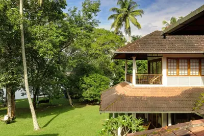 a house with a porch and a grass yard at Cranganor History Café & Riverside Château in Parūr