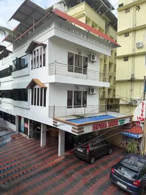 a white building with cars parked in front of it at Siva Inn in Guruvāyūr