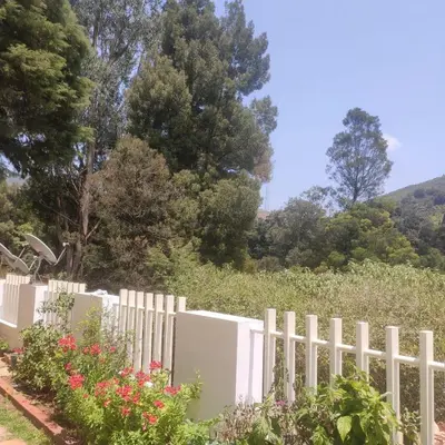 a white fence with flowers and trees in the background at Snowdrops Ooty in Ooty