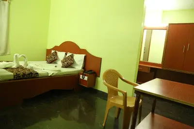 a bedroom with a bed and a table and a chair at Hotel Vijay in Pollāchi