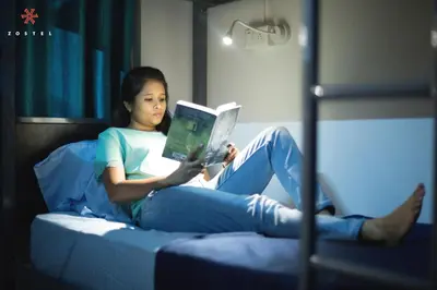 a woman sitting on a bed reading a book at Zostel Mysore in Mysore