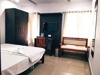 a room with two beds and a chair and a television at Prajapuri Hotel in Trichūr