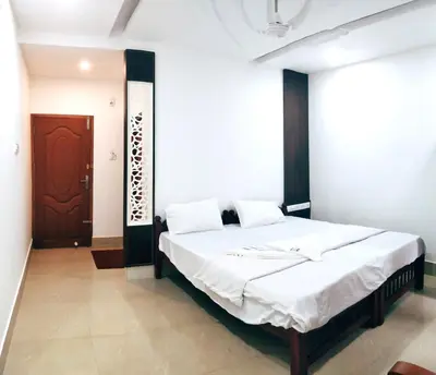 a bedroom with a large bed with white sheets at Prajapuri Hotel in Trichūr