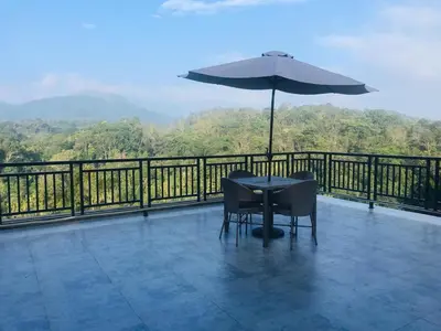 a table and chairs on a balcony with an umbrella at Indeevara Luxury Resort and Spa, Wayanad in Vythiri