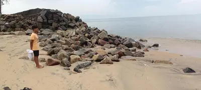 a boy standing on a beach next to a pile of rocks at Swasthigriha's Beach Homestay, Cherai in Cherai Beach