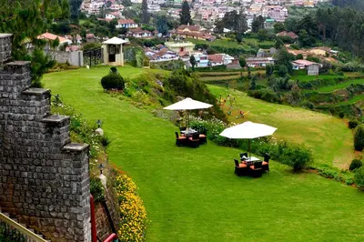 a garden with tables and umbrellas on a green field at Sinclairs Retreat Ooty in Ooty