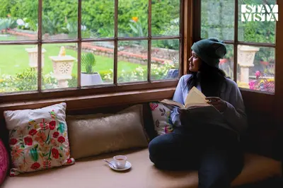 a woman sitting on a couch reading a book at Greenwood Bungalow Heritage In the heart of Ooty in Ooty