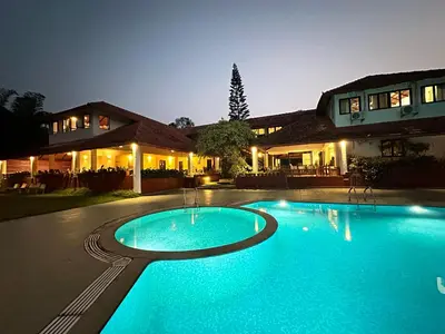 a swimming pool in front of a house at night at Kadkani River Resort Coorg in Siddapur