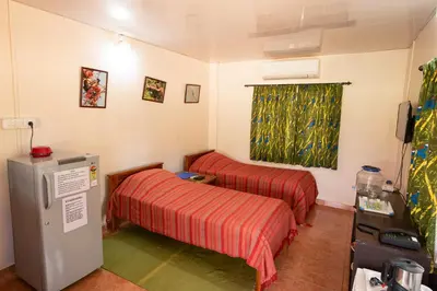 a small room with two beds and a refrigerator at Bamboo Banks Farm & Guest House in Masinagudi